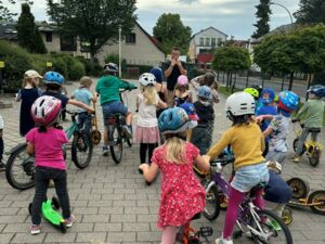 Viele Kinder mit Fahrrädern, Rollern. Die meisten tragen einen Fahrradhelm.