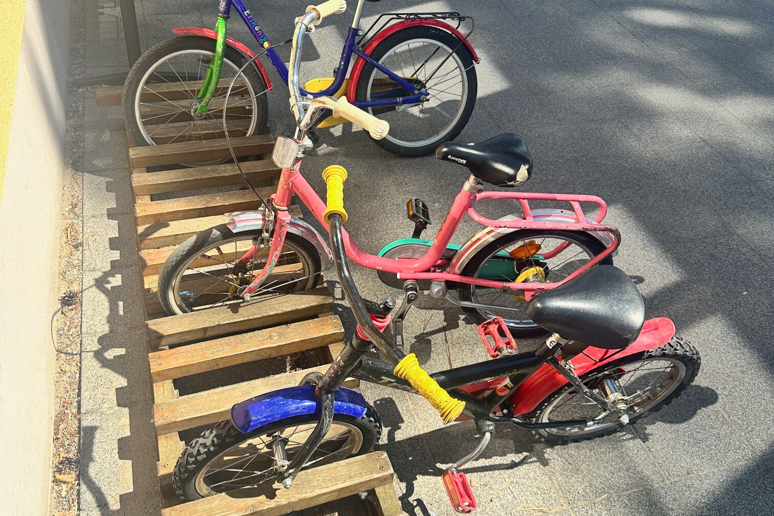 Eine halbierte Europalette dient als Kinderfahrradständer. 3 Räder sind geparkt.