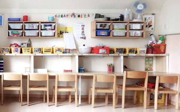 Freizeitraum. Eine Stuhlreihe an einer Wand zu Wand hinblickend. Mit Tisch und darüber Regalen mit Aufbewahrungsboxen und -körben.
