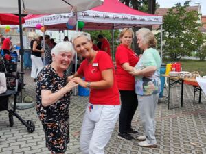 Zwei Helferinnen in roten AWO T-Shirts tanzen fröhlich mit zwei alten Damen. Die Tanzenden im Vordergrund lächeln in die Kamera.