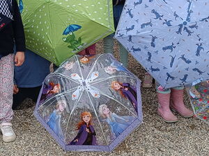 Kinder auf einen Spielplatz vor einer Rutsche. Viele bunte Regenschirme verdecken die Kinder.