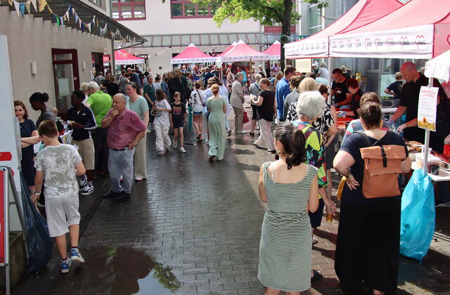 Viele Menschen auf dem Gelände. Essensstand mit roten AWO Pavillons überdacht. Gebäude rahmen das Gelände ein.