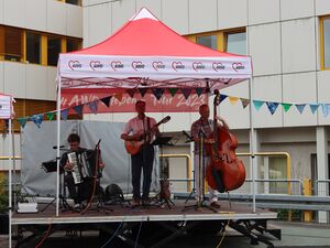 Bühne. Darau ein roter AWO Pavillon und eine dreiköpfige Band Gitarre, Kontrabass und Akkordeon.