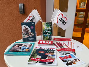 Ein weißer Stehtisch vor einem Gebäude mit Info-Material der  AWO.