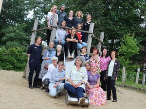 Gruppenfoto von Erwachsenen auf einem Spielplatz und Klettergerüst mit Rutsche. 20 Personen.