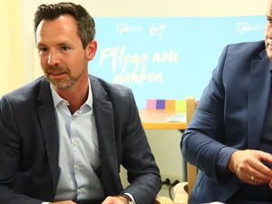 Zwei Männer in Anzügen sitzen nebeneinander.