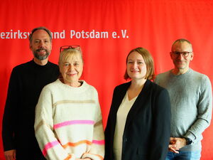 Gruppenfoto vor roter Wand. Zwei Männer hinten außen zwei Frauen vorne mittig. Alle lächeln in die Kamera.