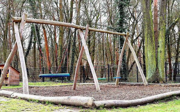 Spielplatz: Schaukeln. Dahinter Bäume.
