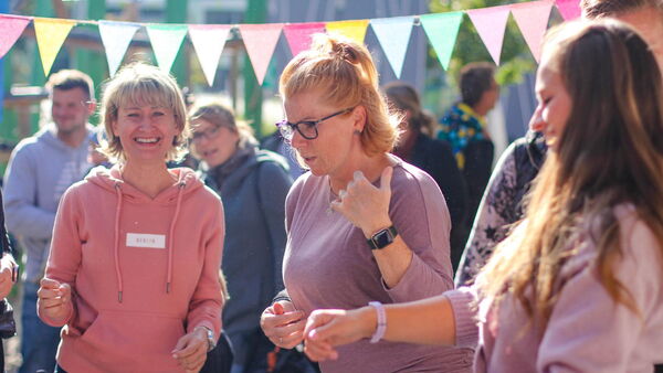 Erzieherinnen. 3 Frauen lachen und albern rum. Draußen Sonne scheint. Bunte Wimpel sind aufgehängt.