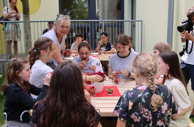 Draußen. Kinder sitzen um einen Tisch und essen Erdbeeren.