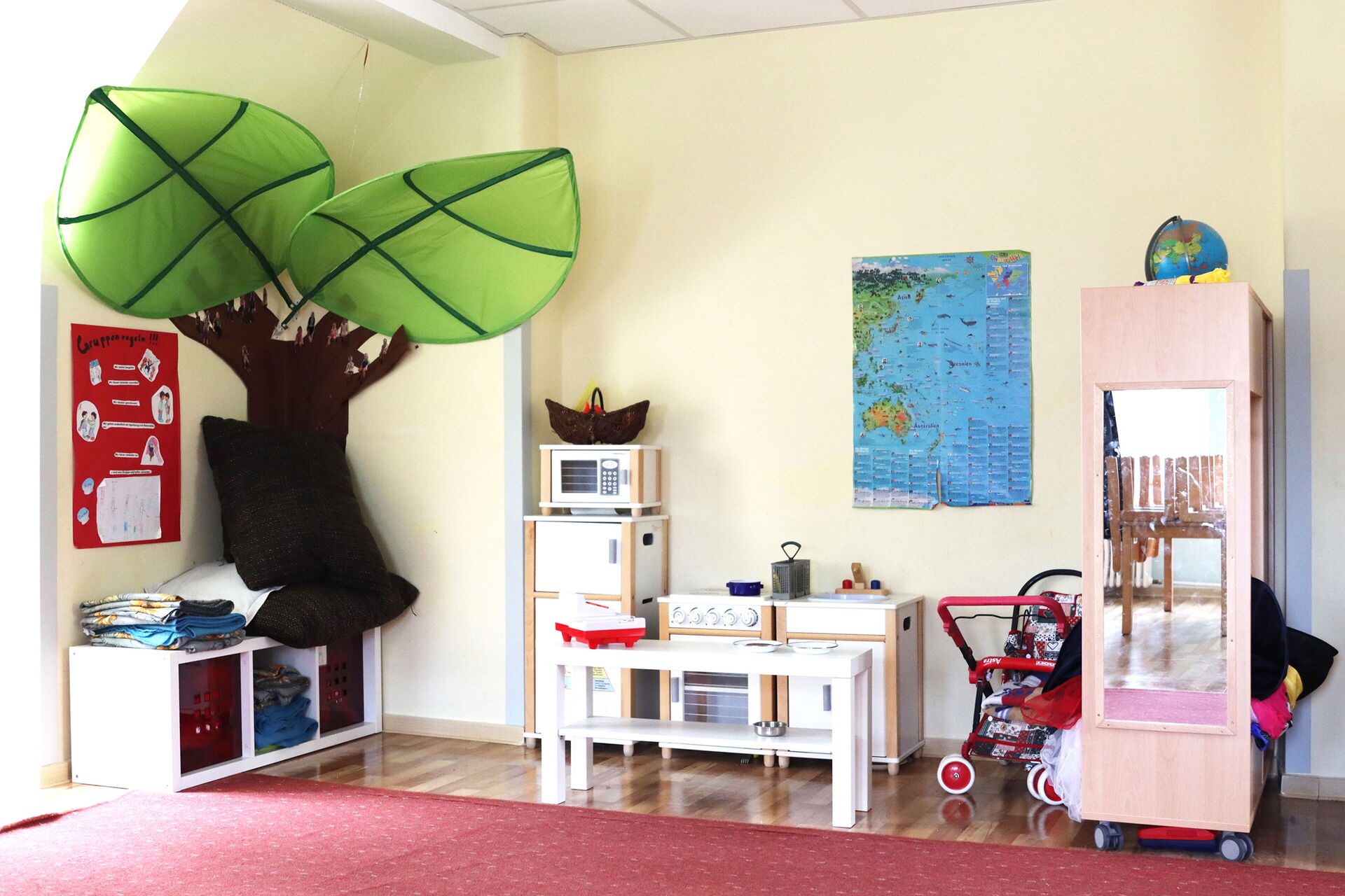Kinderküche mit Herd, Spüle und Mikrowelle. Rechts daneben ein Puppen Kinderwagen und eine Garderobe.