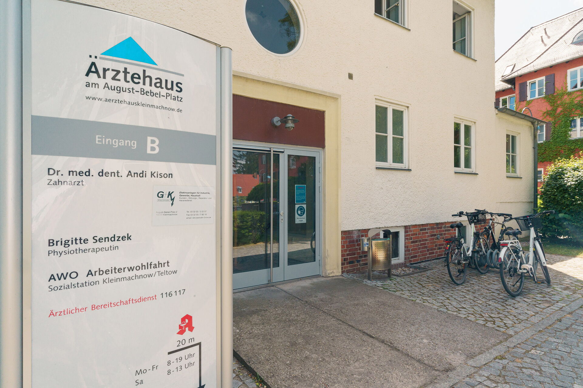 Eingang vom Ärztehaus, ohne Stufen. Schild vom Ärztehaus steht draußen links neben dem Eingang.
