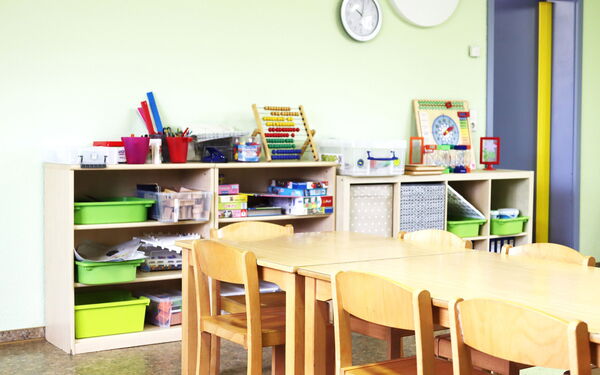 Spielzimmer. Raum mit hellen Wänden. Regale stehen an der Wand. Brettspiele sind im Regal. Auf dem Regal: Rechenschieber, eine Lernuhr und anderen Dinge.