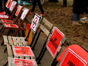 Viele Klappstühle bilden eine Reihe. Sitzflächen und Rückenlehnen sind mit Warnschildern und Sprüchen beklebt.