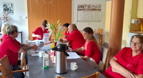 Team in roten AWO Shirts sitzt an einem Tisch mit Unterlagen und Kaffee. Team Sitzung.