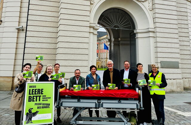 vor dem Fortuna Portal. Ein leeres Pflegebett, ein großes grünes Schild und 10 Menschen mit grünen Karten, mit Aufschrift.