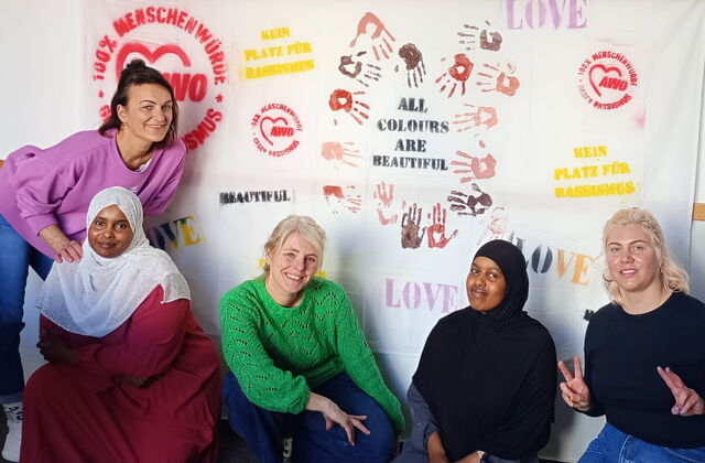 Mitarbeiterinnen und Besucherinnen des interkulturellen Familiencafés vor einem selbst gestalteten Plakat mit Schriftzügen, die ein Zeichen setzen gegen Rassismus und für Vielfalt
