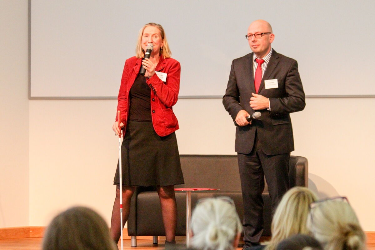 Dörte Maack, Autorin und Moderatorin, steht mit Blindenstock auf der Bühne und moderiert den Vortrag eines Potsdamer Unternehmers an.
