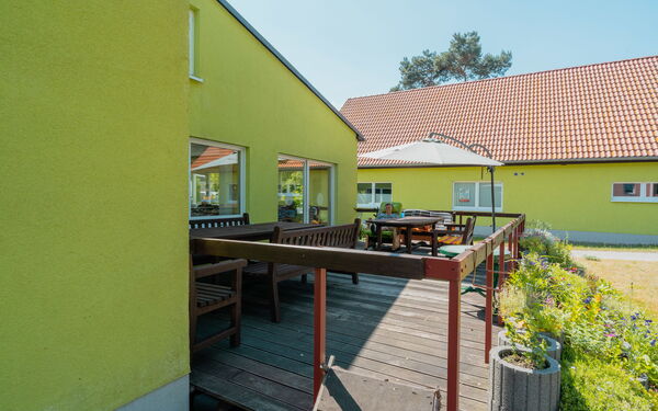 Terrasse mit Sonnenschirm, Tischen und Bänken eines hellgrünen Hauses.