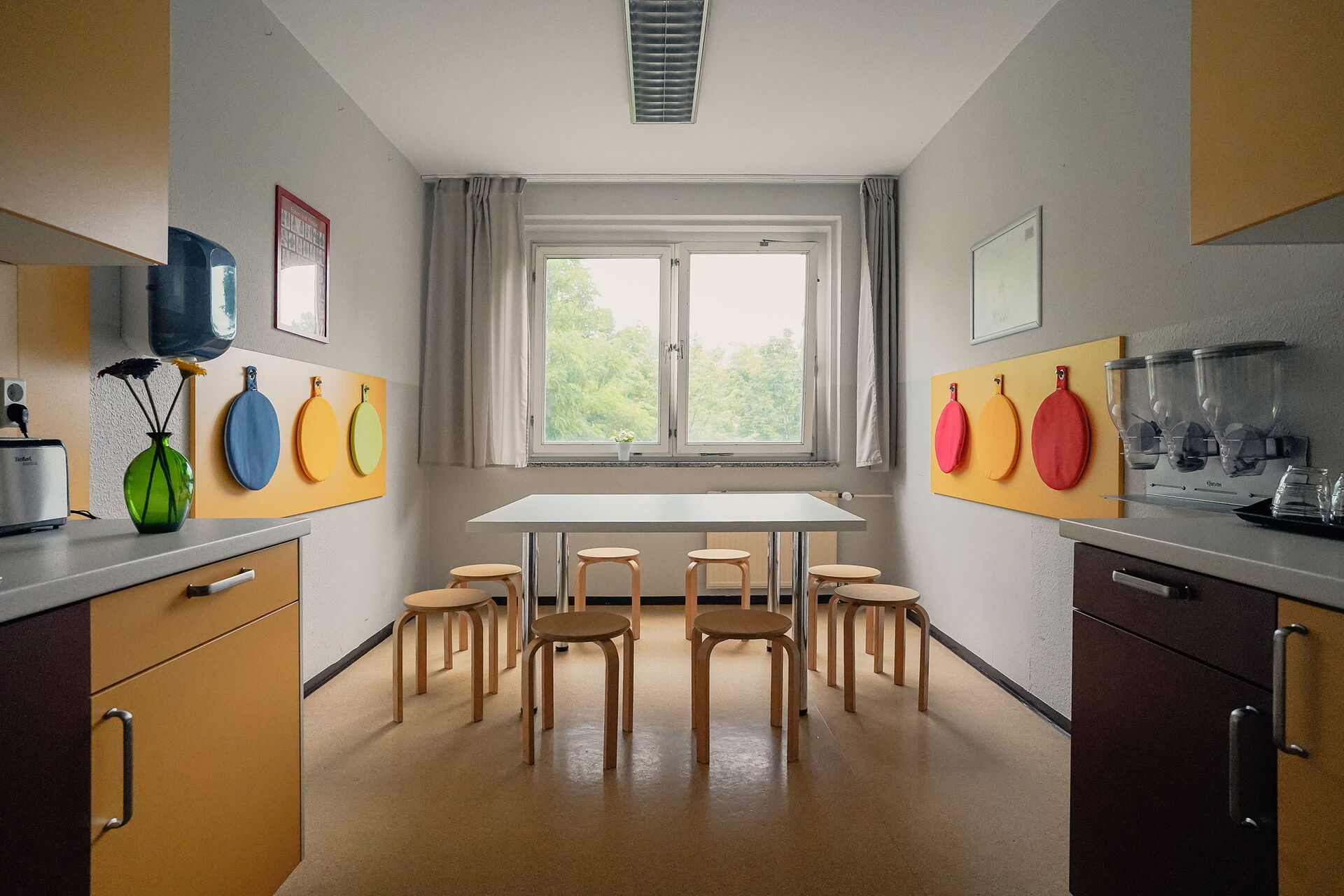 Küche mit großen Tisch mit 8 Hocker rings rum. Großes Fenster lässt Licht hinein.