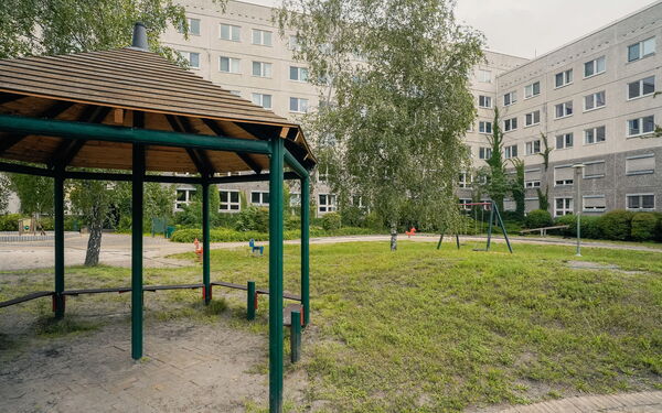 Draußen. Spielplatz, Schaukel, Wippe. Umrahmt von einem Gebäudekomplex.