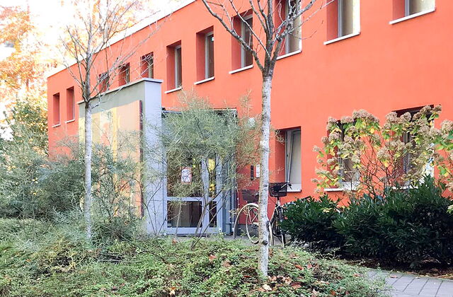 Rotes Gebäude. Vom Gehweg, sind vier Stufen zu einem Weg der zum Eingang des Gebäudes führt.