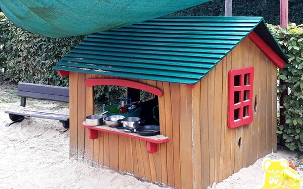 Ein kleines Holzhaus im Garten. Auf dem Fensterbrett Töpfe und Pfannen. Sandkasten davor.
