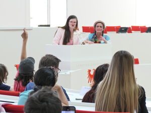 Politikerin und Clownin am Rednerpult. Kinder in Saal.