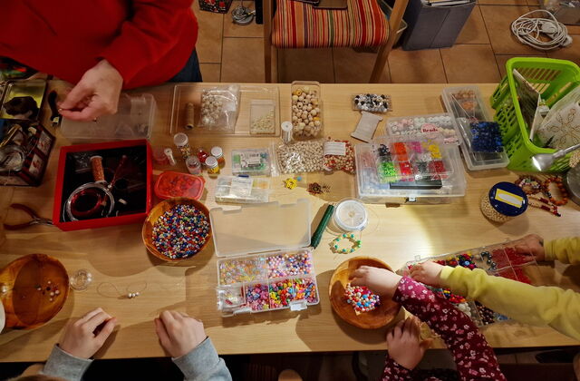 Tischplatte von oben mit vielen Schalen und Dosen mit bunten, holz Perlen. Kinder Basteln Ketten und Armbänder.