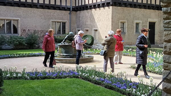Angelegte Blumenbeete mit Frühblühern entlang der Wege, 5 Frauen der Gruppe sehen sich um. Ein großes Gebäude.