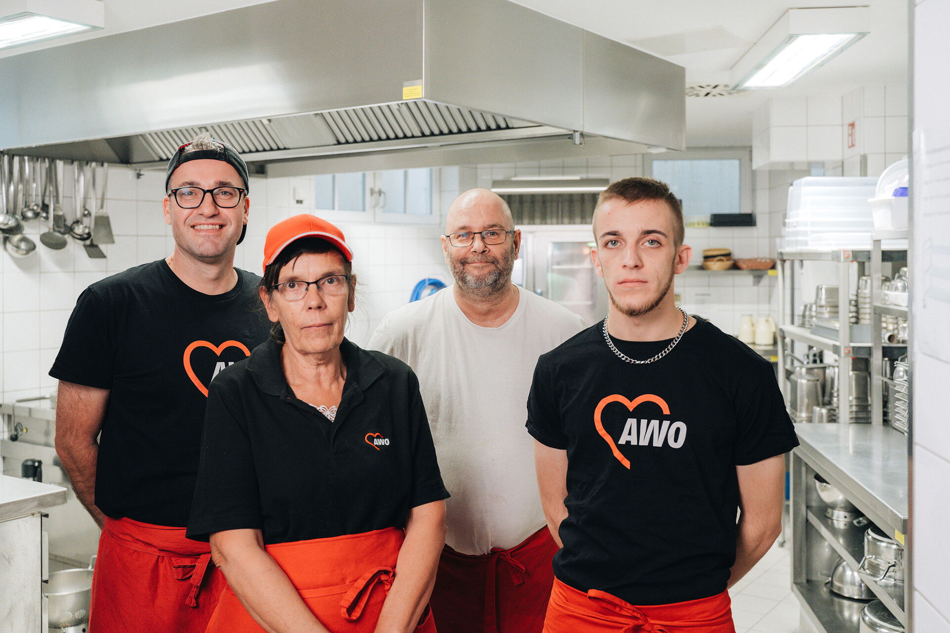 Teamfoto. In einer Großküche. Drei Männer und eine Frau stehen und lächeln in die Kamera.