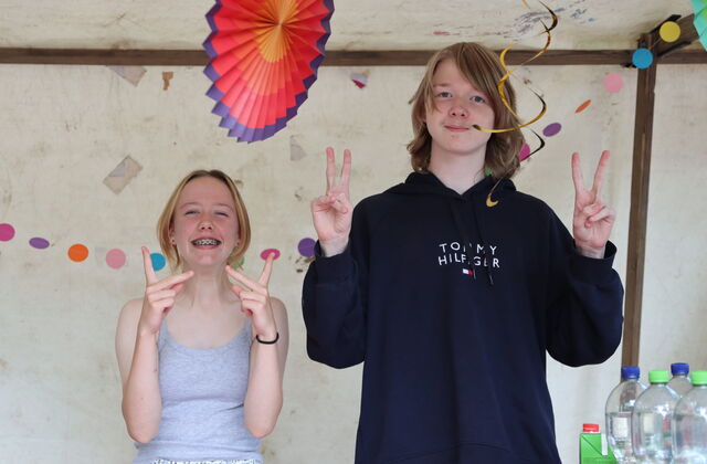 2 Kinder / Jugendliche stehen nebeneinander und grinsen in die Kamera.