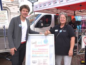 Mann und Frau am AWO-Stand zwischen ihnen der Aufsteller: "Lust auf Ehrenamt?" Mann trägt weißes T-Shirt und graue Anzugjacke. Frau streckt den Daumen noch oben, sie trägt ein schwarzes Poloshirt und hat graue schulterlange Haare.