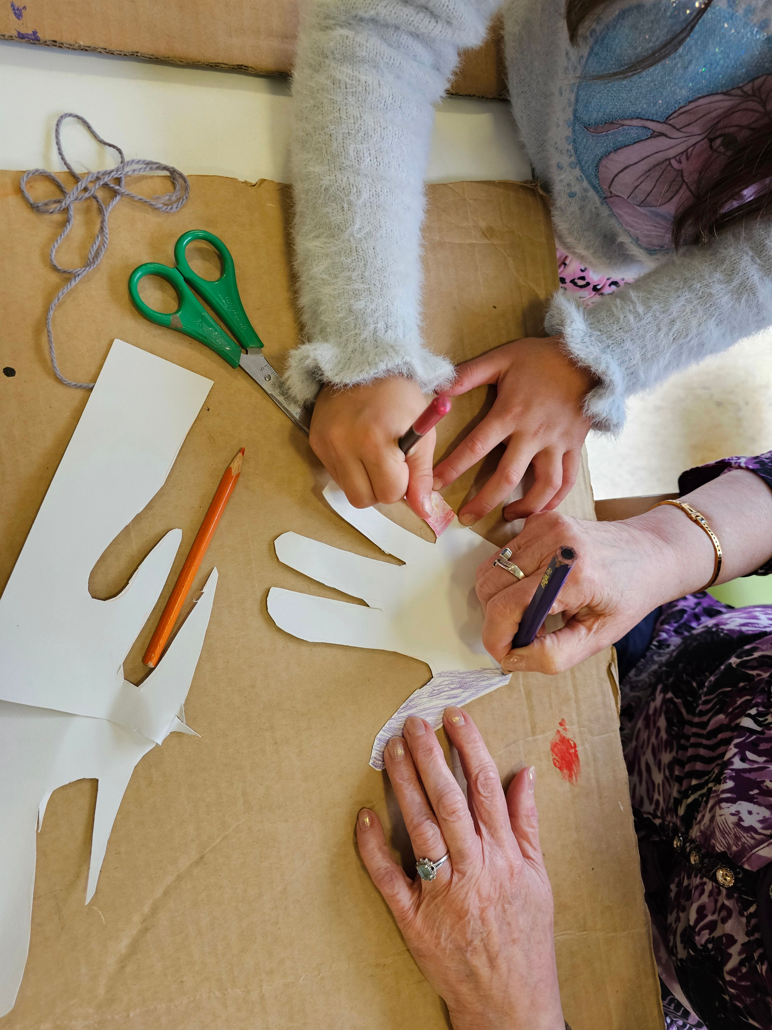 Ein Kind und ein älterer Mensch malen gemeinsam eine Hand aus. Nur die Hände sind zu sehen.