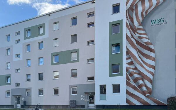 Grau Weißes 5 Geschosswohnhaus. Von der WBG eG Wittstock/Dosse steh am Gebäude.