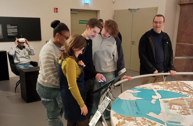 4 junge Menschen stehen im Museum an einem Monitor der bei einem großen, dreidimensionalen Brandenburg-Relief im Museum, das die topografische Landschaft mit Hügeln und Seen zeigt.