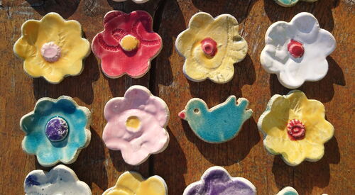 Das Bild zeigt kleine, bunte selbstgetöpferte Blumen und Vögel