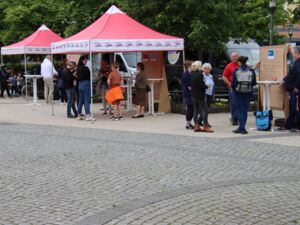 Draußen. 2 AWO Pavillons. Unter einem steht eine kleine Gruppe Menschen. Mehrere Stationen mit Flipcharts sind aufgebaut. Kleine Grüppchen haben sich an den den einzelnen Stationen zusammengefunden.