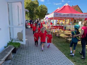 Kleine Kinder in roten T-Shirts kommen einem Weg heran gelaufen auf den Fotografen zu. Draußen, die Sonne scheint, AWO-Pavillons und Biertischgarnituren.
