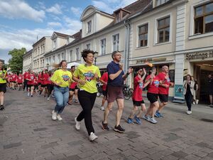 Eine große Gruppe Menschen in roten T-Shirts und schwarzen kurzen Hosen, läuft / rennt eine Straße hinauf. Daneben der Potsdamer Oberbürgermeister in Sportkleidung rennt mit.