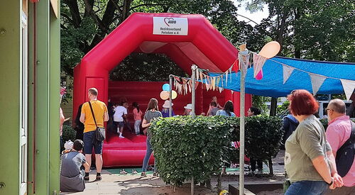 Rote Hüpfburg oben mit AWO Potsdam Logo. Kinder sind auf der Hüpfburg. Kinderschuhe stehen davor. Es ist ein sonniger Tag.