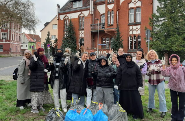 auf dem Bild sind mehrere Frauen aus verschiedenen Herkunftsländern vor dem Gebäude des interkulturellen Familiencafés und lachen in die Kamera. Vor ihnen sind mehrere volle Müllsäcke, die gesammelt wurden