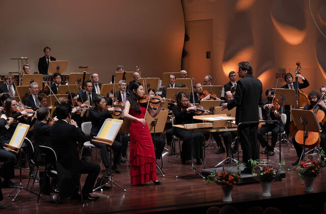 Hier sehen sie ein Orchester mit einer Frau im roten Kleid mit einer Geige