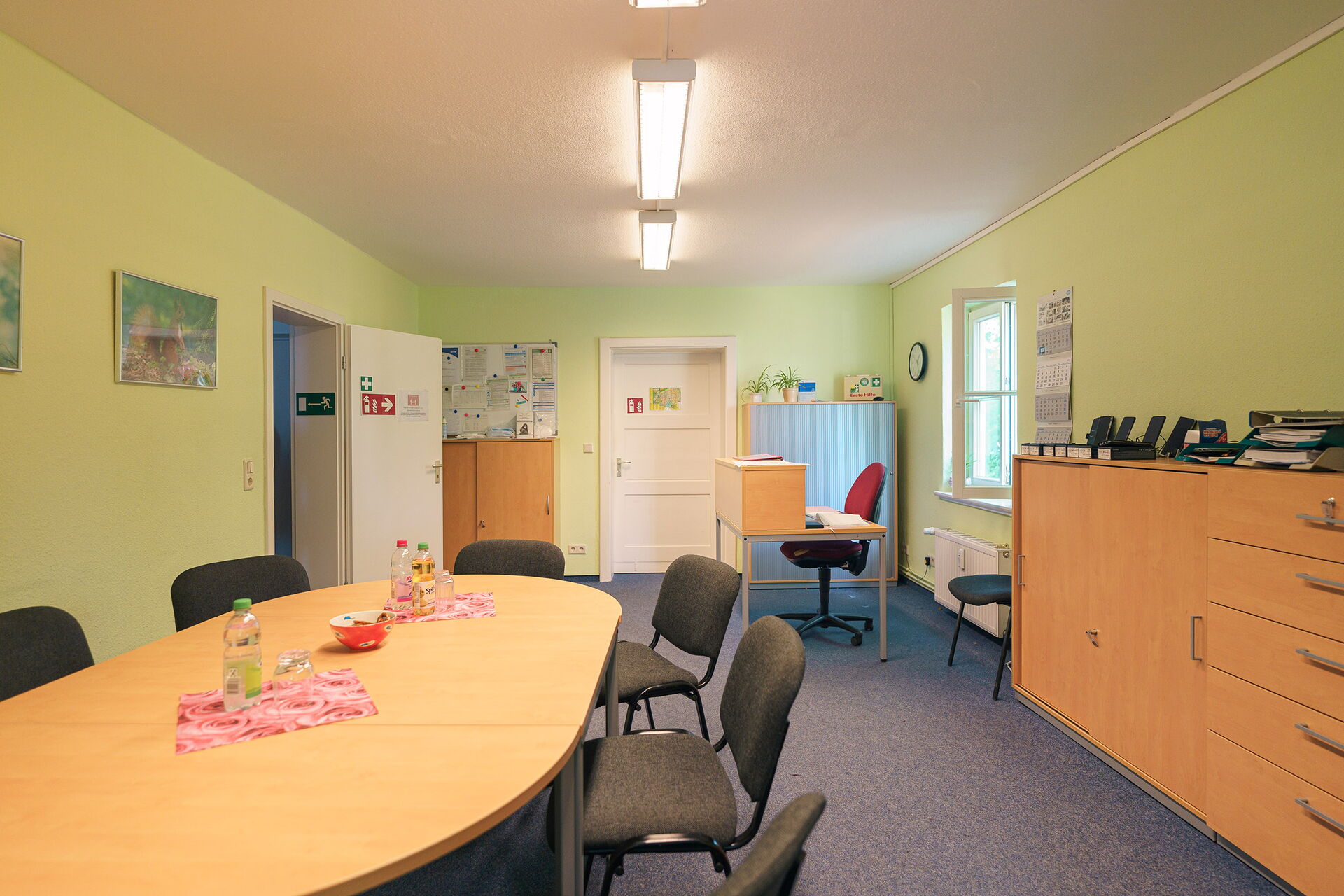 Besprechungsraum. Ovaler Tisch mit 6 Stühlen, rechts an der Wand steht ein Schrank.