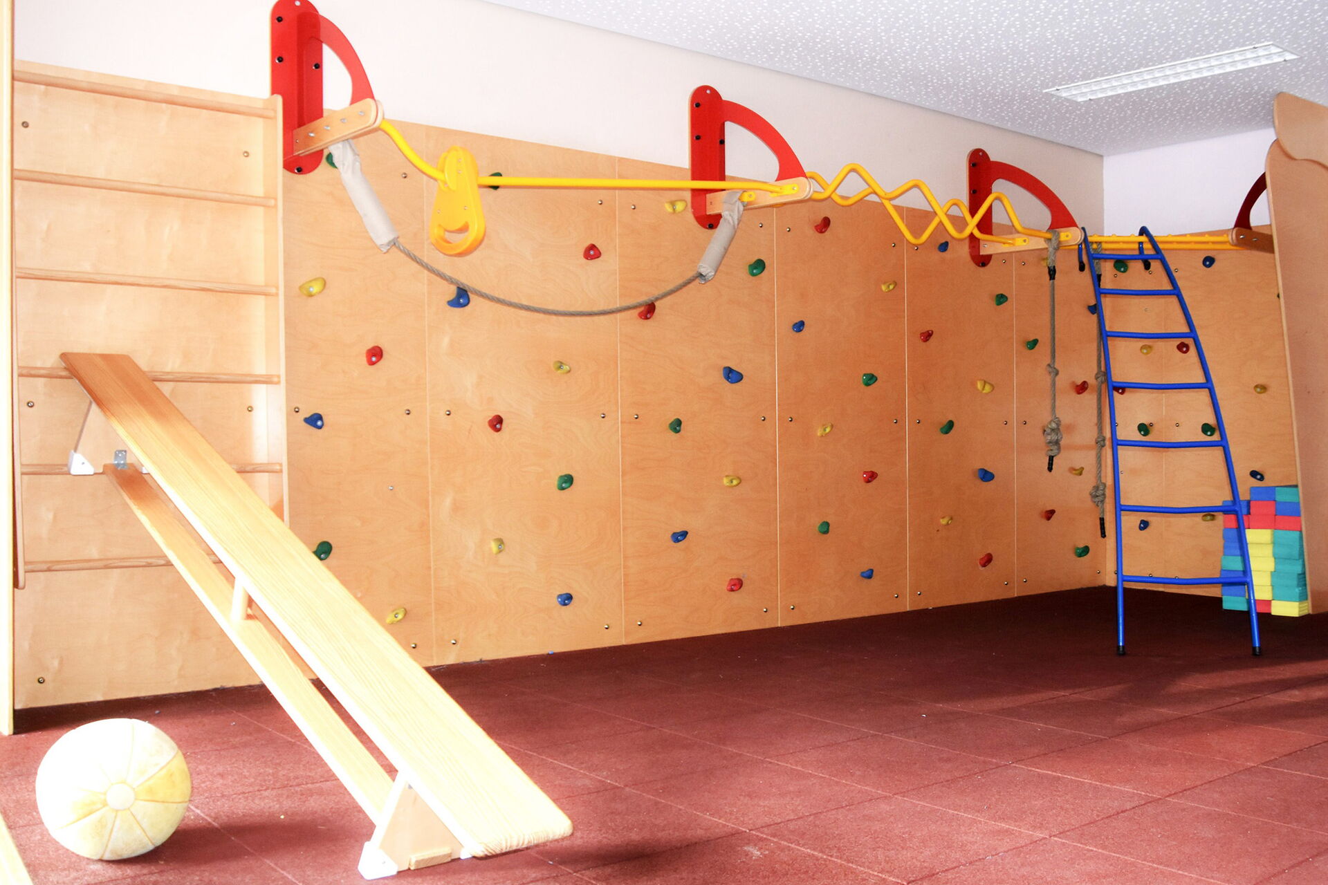 Sportraum. Mit Kletterwand, Sprossenwand, ein Ball liegt auf dem Fußboden, Eine Bank ist an die Sprossenwand gelehnt.