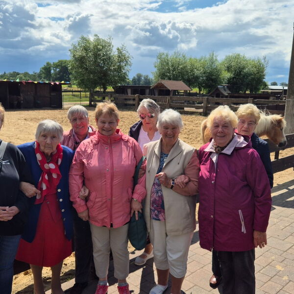 Gruppenbild vor Pferdekoppel. 8 Frauen fröhlich bei sonnigem Wetter.