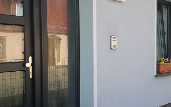 Eingangstür. An der Wand rechts neben der Tür die Klingel und die Hausnummer 12a weiter oben.