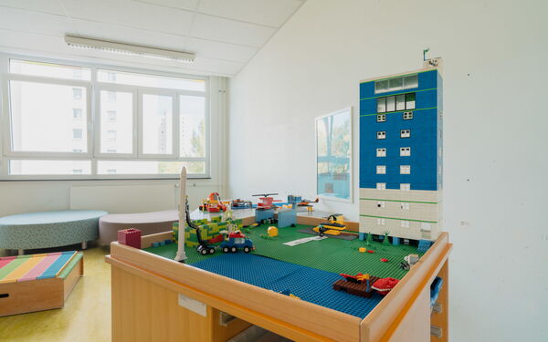 Spielzimmer. Lego Tisch, bebaut mit einem Hochhaus vor dem Bäume stehen, Hubschrauber und ein Baufahrzeug sind auf dem Tisch verteilt.