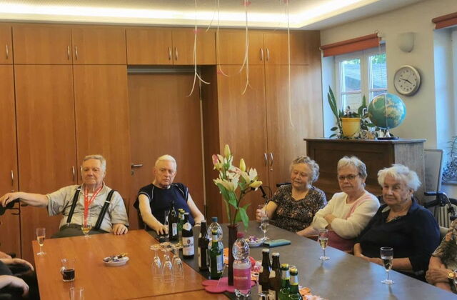 Alte Frauen und Männer an einem großen Tisch. Auf dem Tisch stehen Getränke und Gläser.
