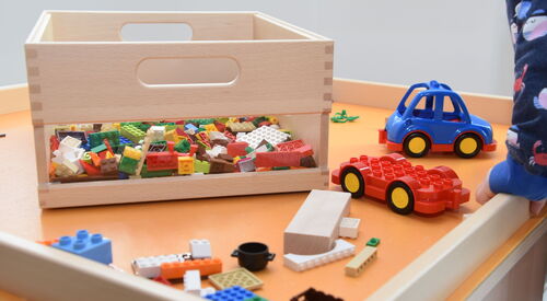 Spieletisch mit Legokiste und kleines blaues Auto.